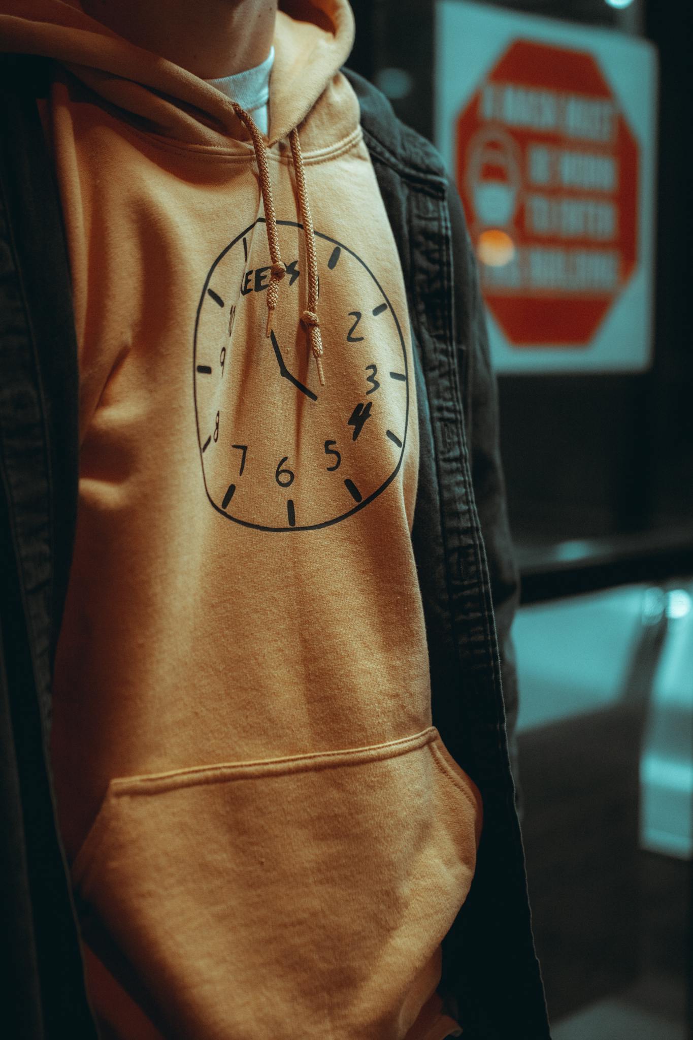 Close-up of a person wearing an orange hoodie with a clock design, showcasing urban style.