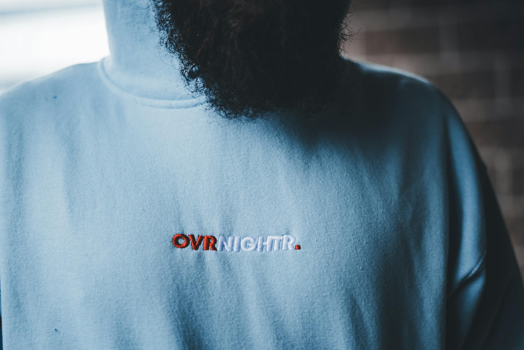 Detailed close-up of a blue hoodie with embroidered text and a partial view of a beard.
